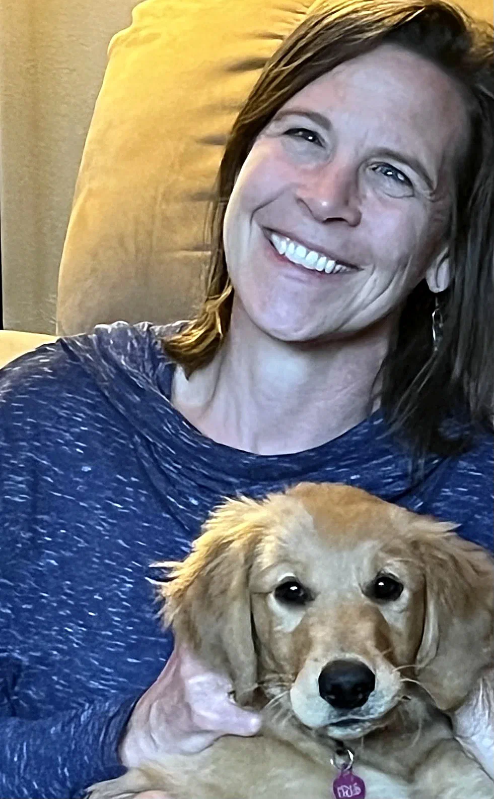 Karna Johnson smiling in an armchair with a golden retriever puppy on her lap